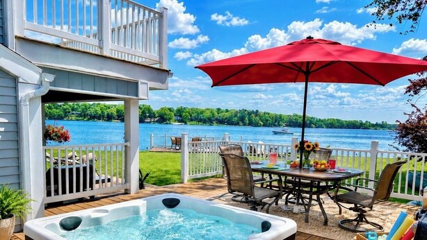 A deck with a hot tub, outdoor furniture, and a view of a lake. - PONTOON BOAT NOW INCLUDED! 7 BEDS, HOT TUB Updated Lakefront Cottage - Book Now (Norton Shores)