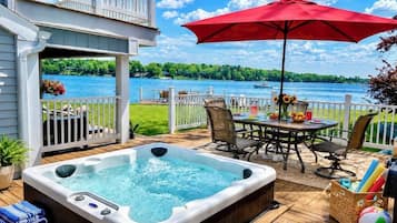 A deck with a hot tub, outdoor furniture, and a view of a lake.