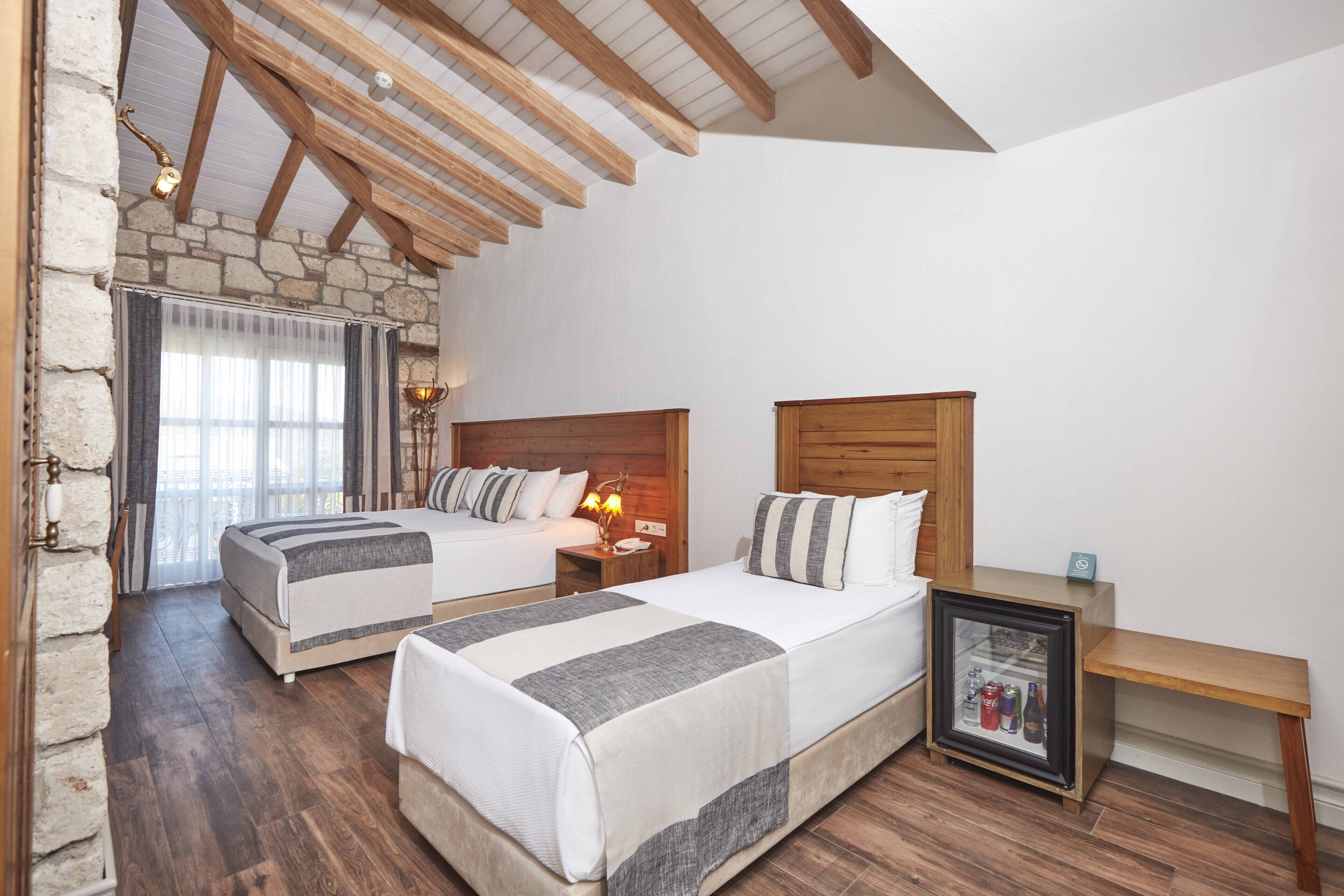 A bedroom with two beds, wooden beams, stone walls, and a small bedside table with a framed picture.