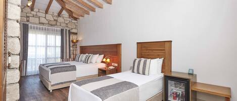 A bedroom with two beds, wooden beams, stone walls, and a small bedside table with a framed picture.