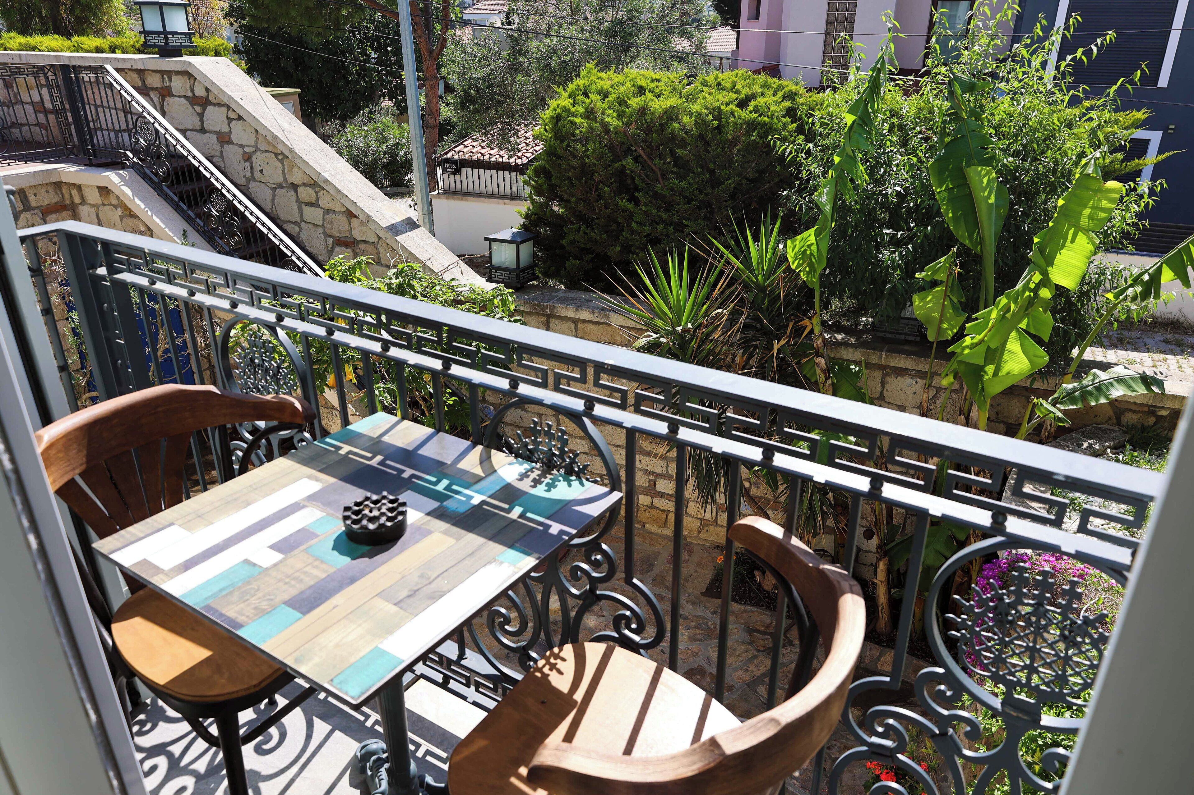 A balcony with a chessboard table, two wooden chairs, and a metal railing.