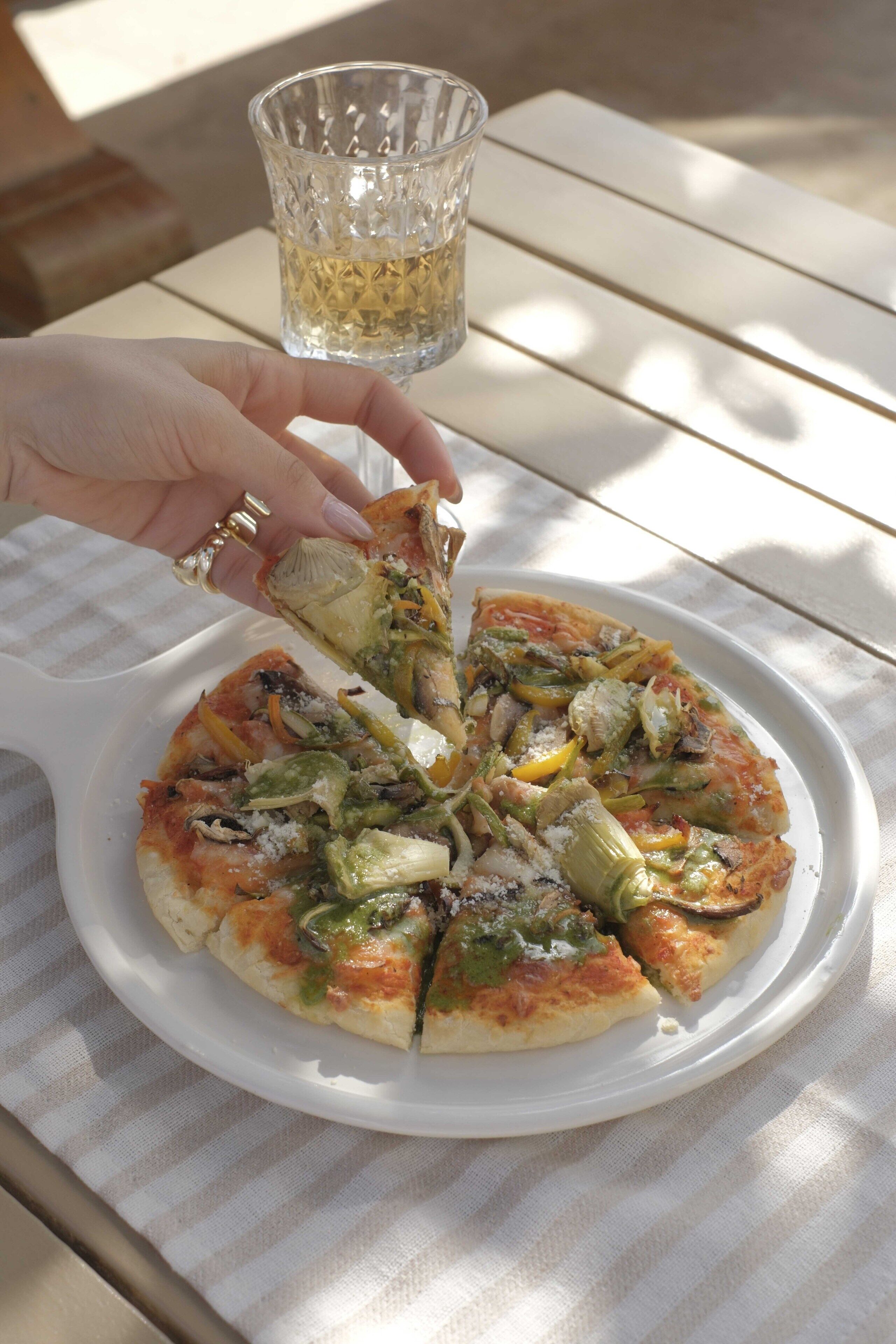A pizza on a white plate with a hand picking up a slice.