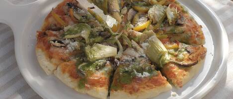 A pizza on a white plate with a hand picking up a slice.