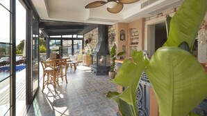 Uma varanda ampla com piscina, área de refeições com mobiliário de madeira e parede de pedra com detalhes decorativos.