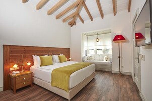 Un dormitorio con cabecera de madera, cama con ropa blanca y un plaid verde, mesita de noche con lámparas y una lámpara de pie roja.