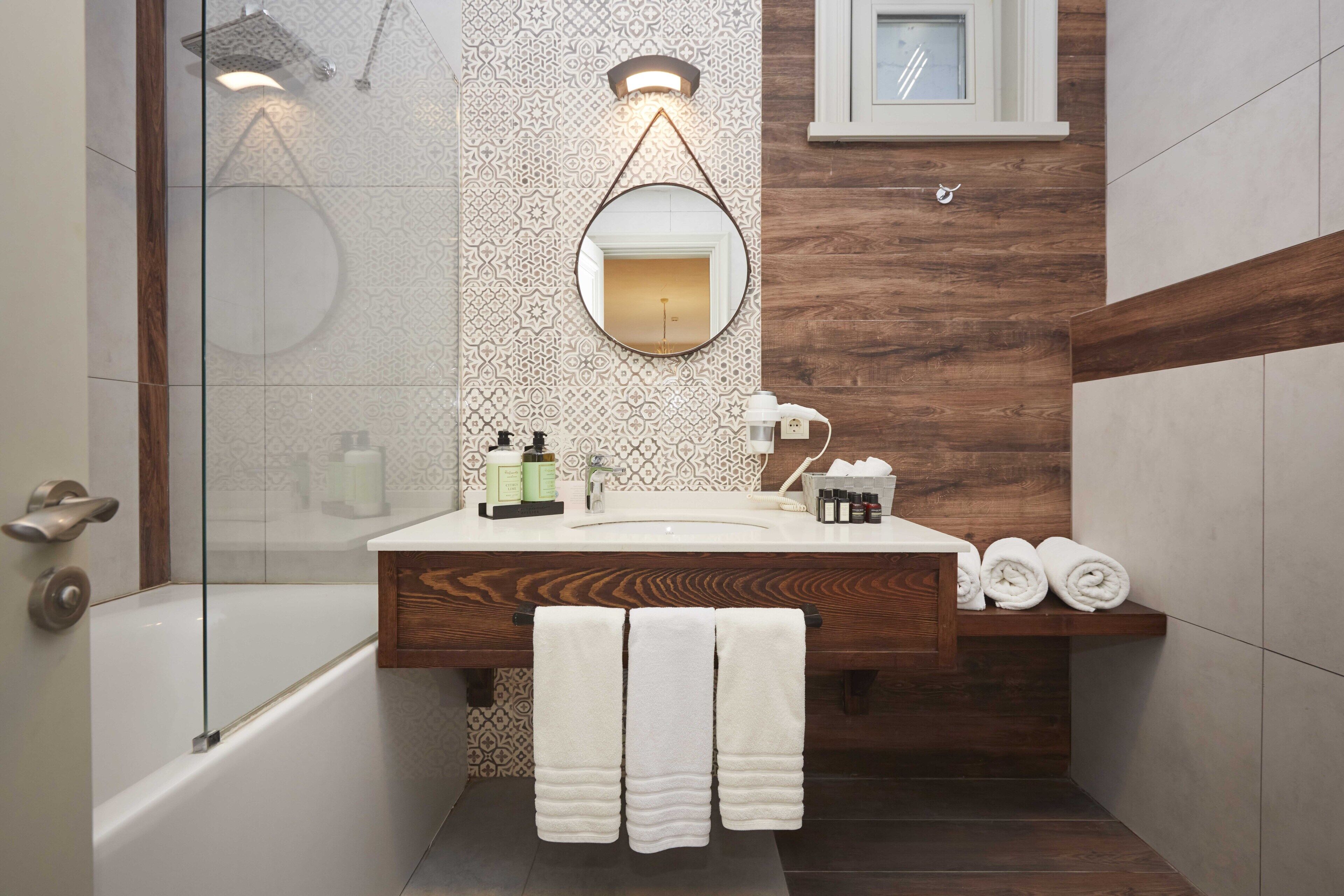 A modern bathroom with a wooden vanity, a round mirror, and a shower area.