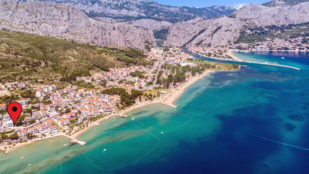 Vista aérea de uma cidade costeira com montanhas ao fundo, uma praia e águas azul-claras.