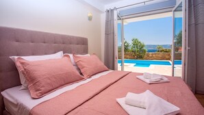 Quarto com uma cama grande, vista para uma piscina e uma parede de pedra.