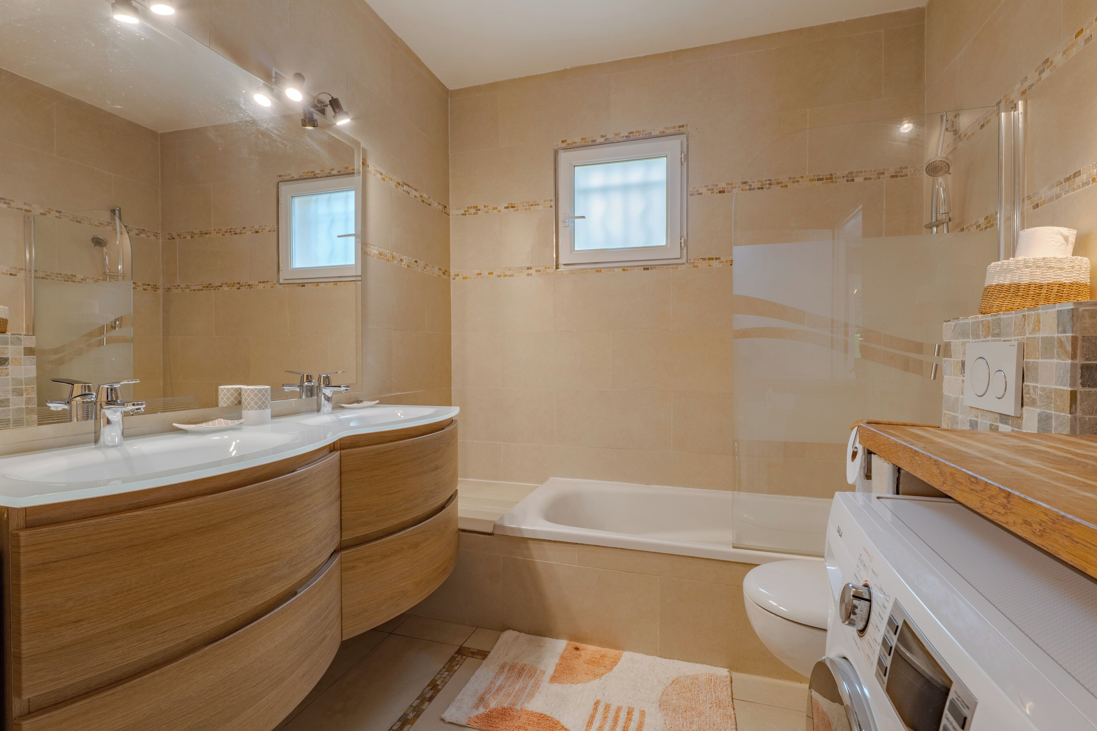 A modern bathroom with a double sink vanity, a bathtub, a toilet, and a washing machine.