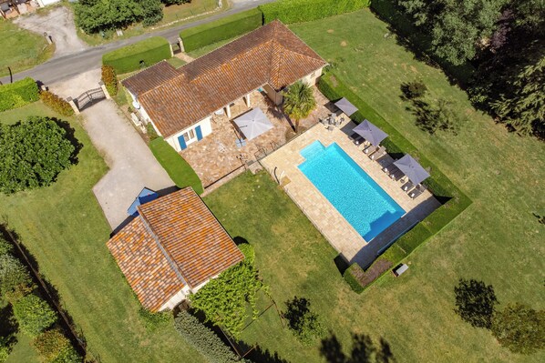 Vista aérea de uma casa com piscina, um edifício separado com telhado telhado e gramado bem cuidado.