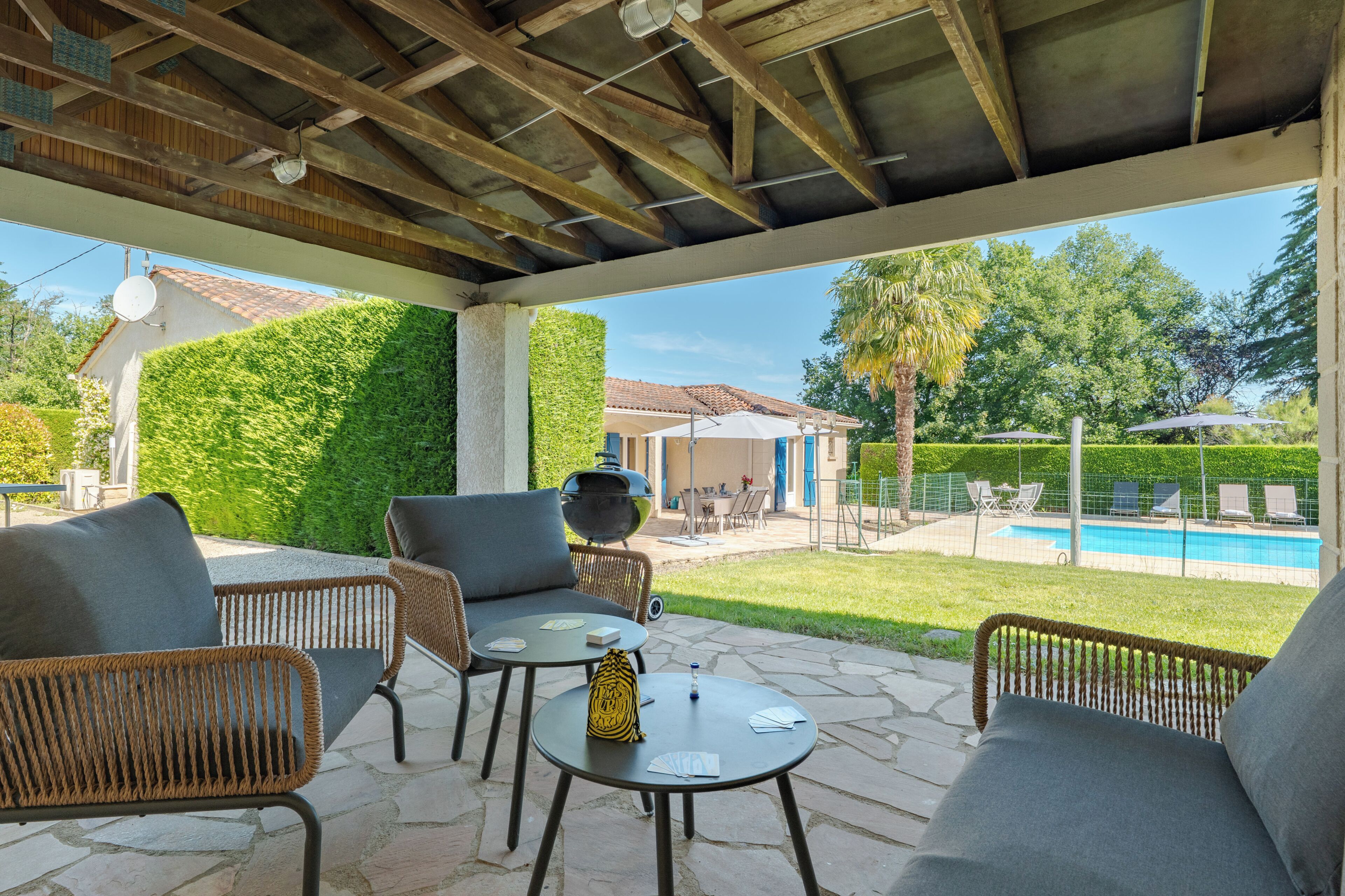 An outdoor patio with wicker furniture, a barbecue grill, and a view of a swimming pool.