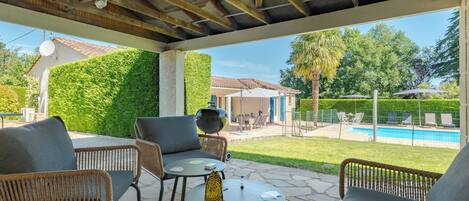An outdoor patio with wicker furniture, a barbecue grill, and a view of a swimming pool.