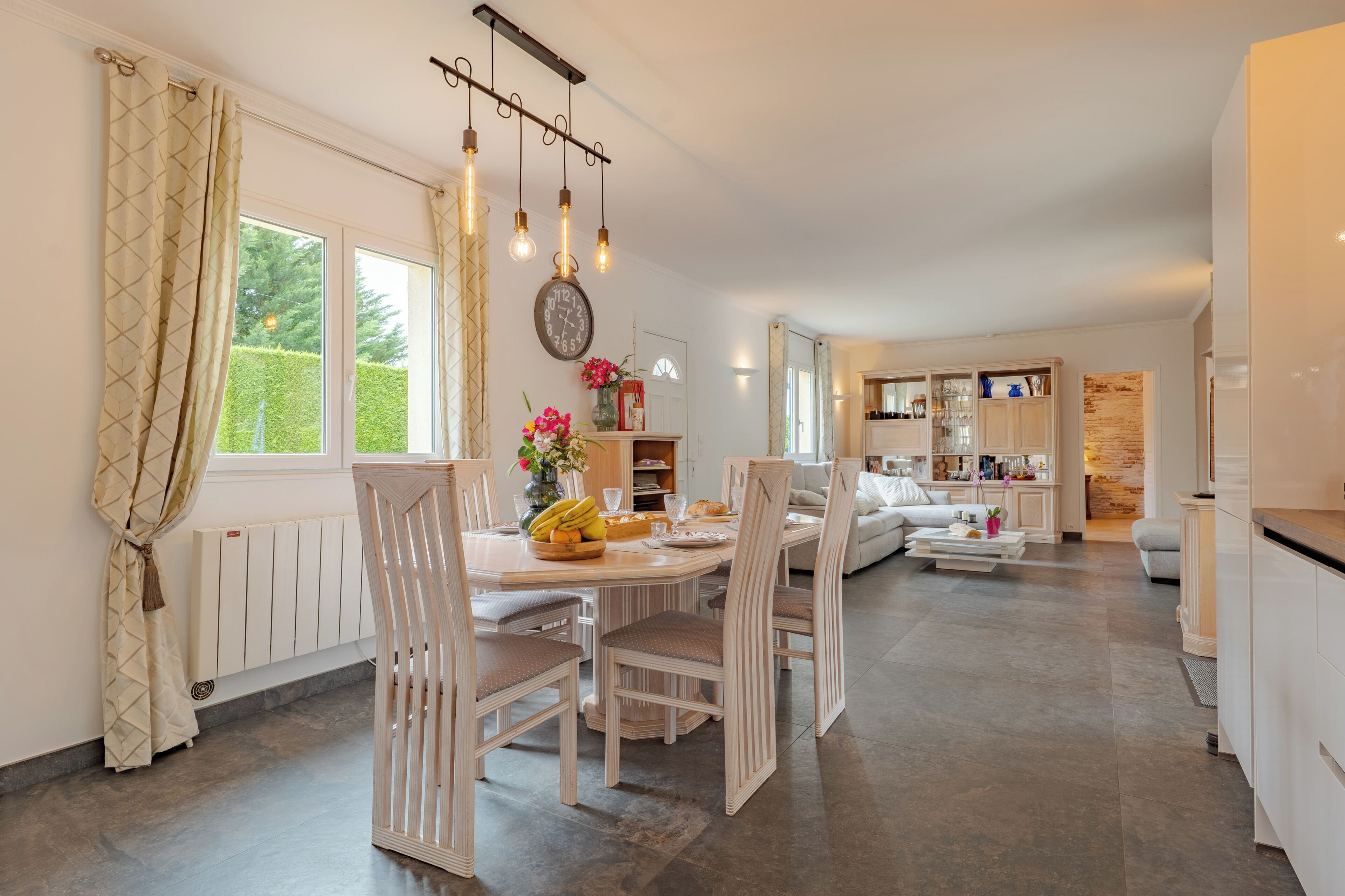 Une cuisine moderne avec un coin repas, des meubles blancs et une grande fenêtre agrémentée de rideaux.