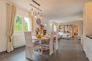 A modern kitchen with a dining area, white cabinetry, and a large window with curtains. - Grauvière is a lovely holiday home (Anglars-Nozac)