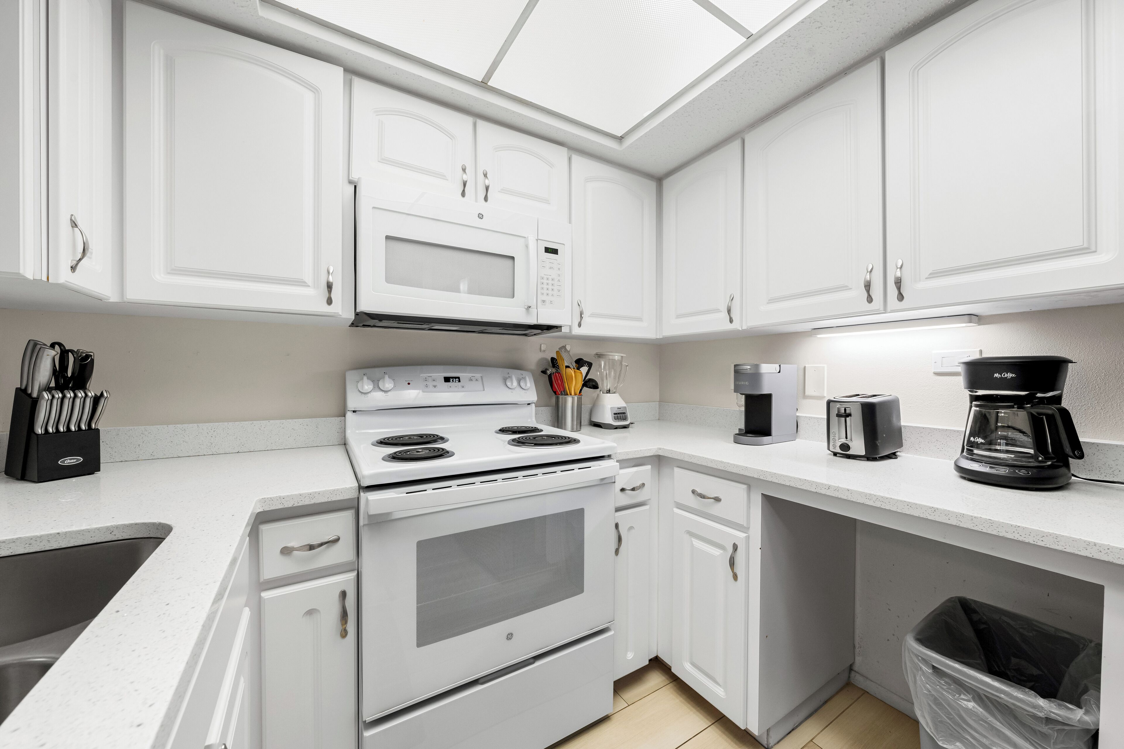 A modern kitchen with white cabinetry, a built-in microwave, a stove, and a coffee maker.