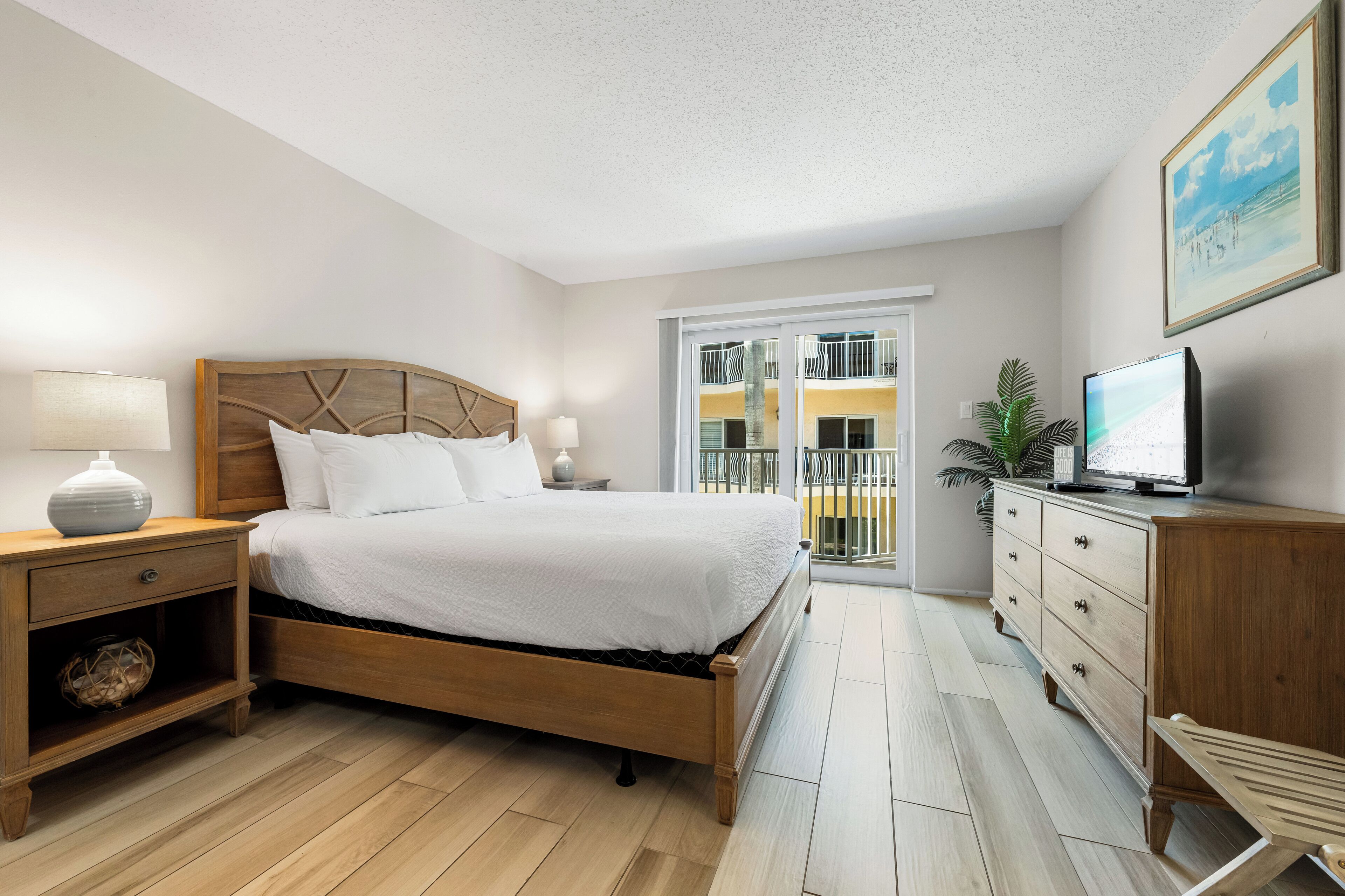 A bedroom with a wooden bed, bedside tables, a TV, and a balcony with a view.