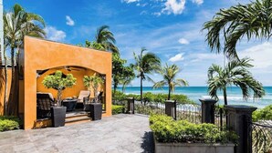 Eine strandseitige Terrasse mit Gartenmöbeln, Palmen und Blick auf den Ozean.