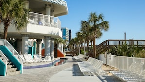 Et resort med pool, liggestole, palmer og en trappe op til en balkon.