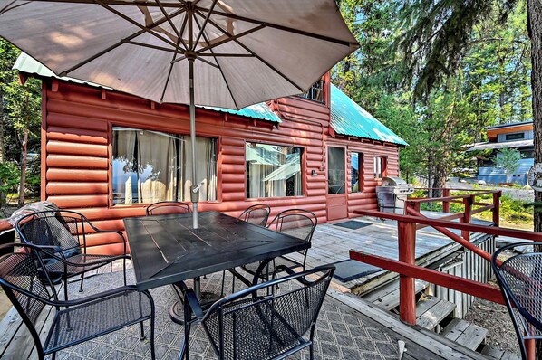 Une cabane en rondins dotée d’un patio comprenant une table et des chaises, un parasol et un barbecue.