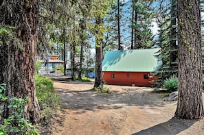 A cabin surrounded by tall trees, with a dirt path leading to it. - Vintage 1940s McCall Lakefront Cabin |Boat Slip (McCall)