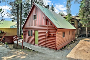 Une cabane en rondins avec une porte verte, un petit porche et un toit en métal.
