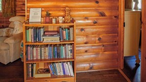 A cozy log cabin interior with a wooden bookshelf filled with books, a framed picture on the wall, and a small decorative item. - Vintage 1940s McCall Lakefront Cabin |Boat Slip (McCall)