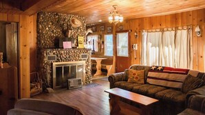 A cozy cabin interior with a stone fireplace, wooden walls, a leather sofa, and a dining area. - Vintage 1940s McCall Lakefront Cabin |Boat Slip (McCall)