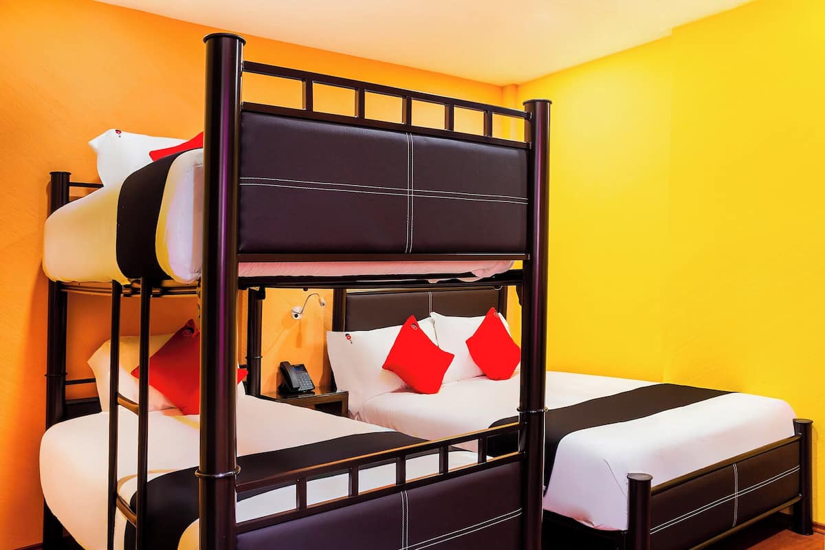 Una cama litera con estructura negra y ropa de cama blanca, una mesita de noche con lámpara y una almohada roja.