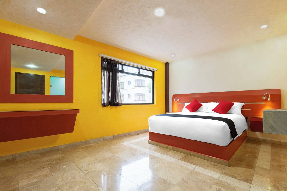 Una habitación de hotel con una cama grande, un espejo, una ventana con cortinas y un piso de baldosas.