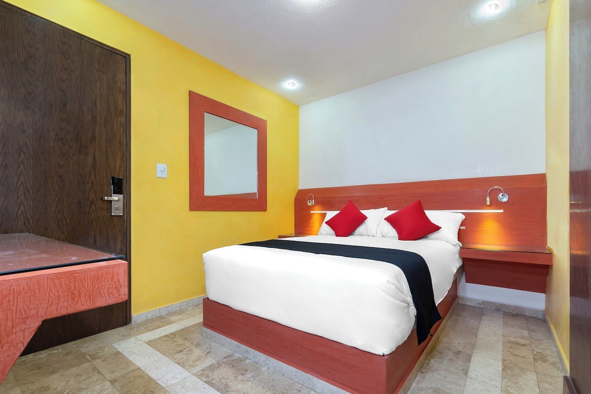 Una habitación de hotel con cama, mesita de noche y un espejo en la pared.