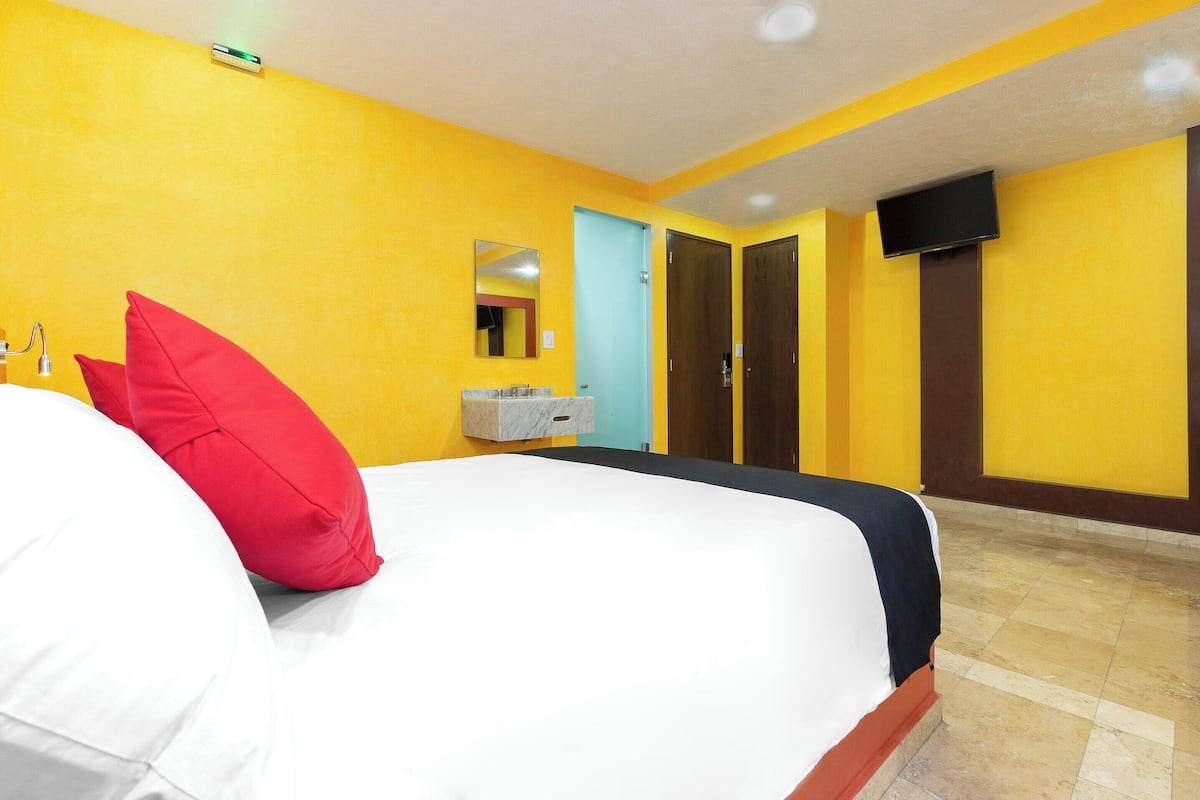 Habitación de hotel con cama, baño con espejo y televisor montado en la pared.