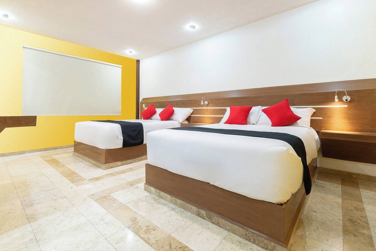 Habitación de hotel con dos camas, cabecero de madera y una ventana grande con persiana blanca.