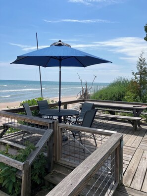 A wooden deck with a table and chairs, overlooking the ocean.