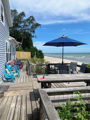 A wooden deck with outdoor seating, a blue umbrella, and a view of the beach.