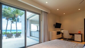 Ein Hotelzimmer mit Bett, Schreibtisch, Stuhl, Fernseher und Blick auf den Strand und Palmen.