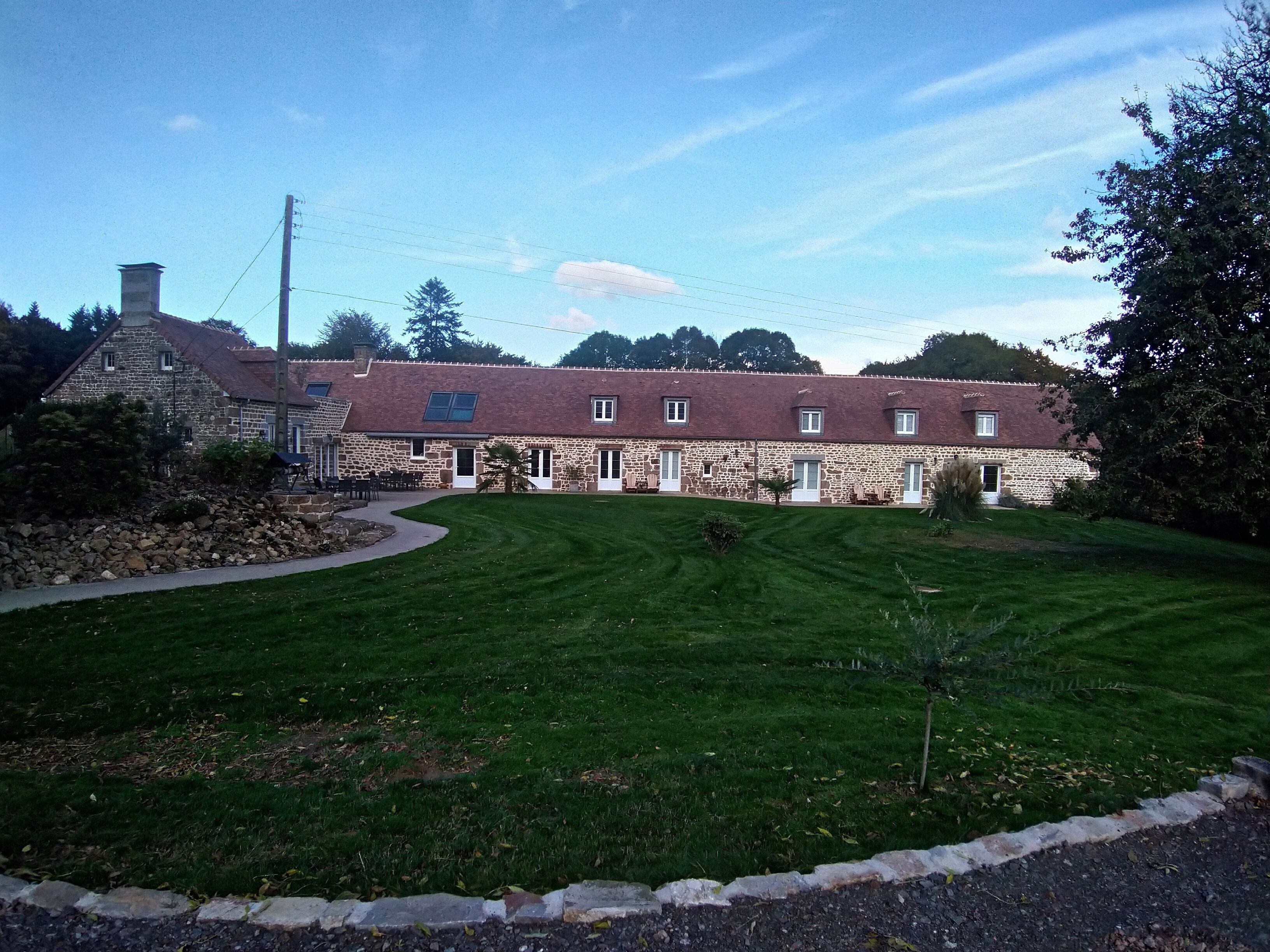 A stone building with a red roof, a stone chimney, and a well-maintained lawn.