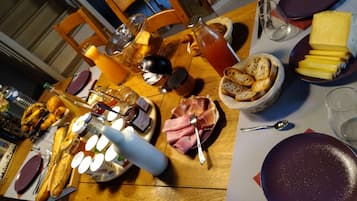 Een eettafel gedekt met diverse soorten eten, zoals brood, kaas en een fles wijn.