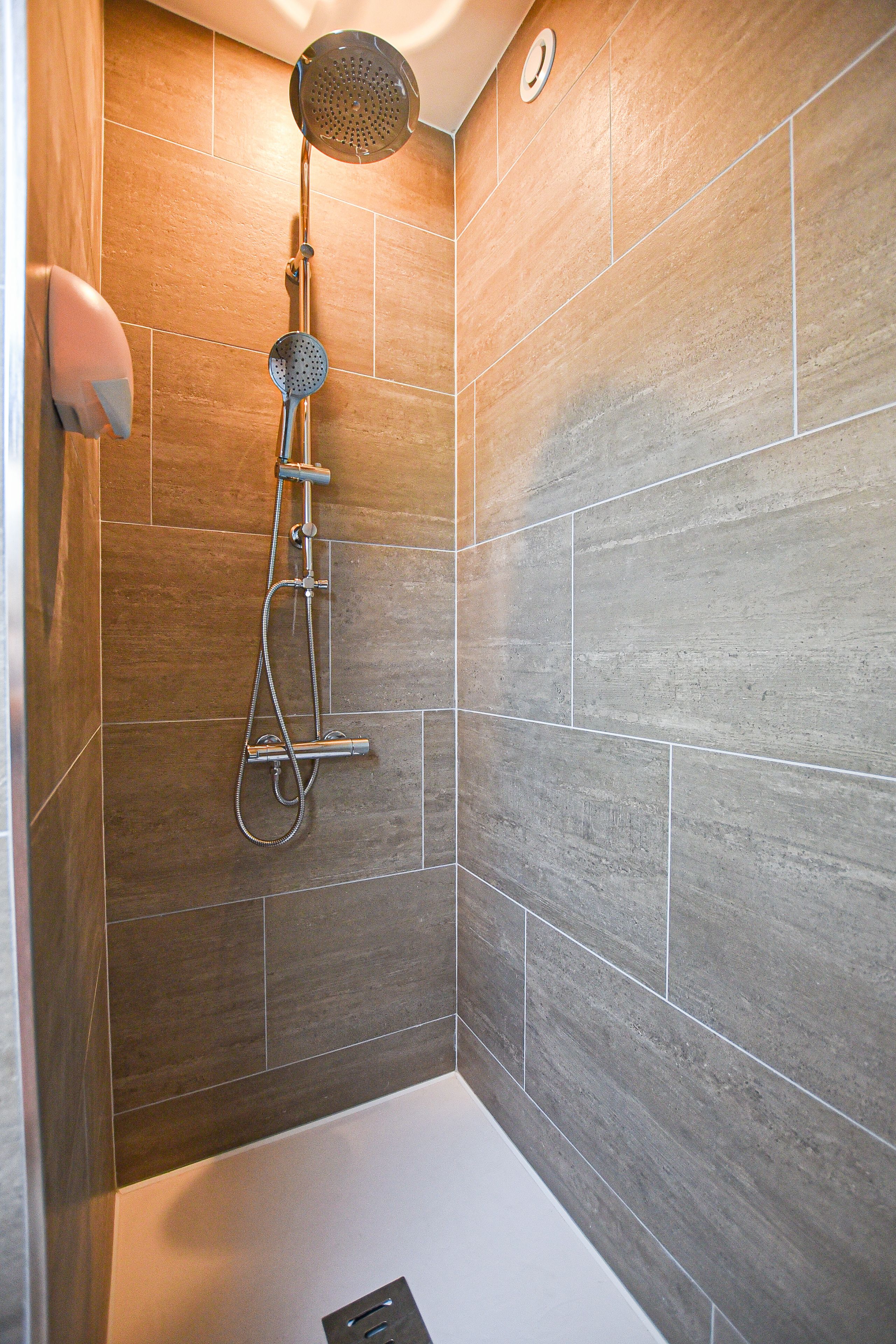 A shower with a handheld showerhead and a wall-mounted faucet.