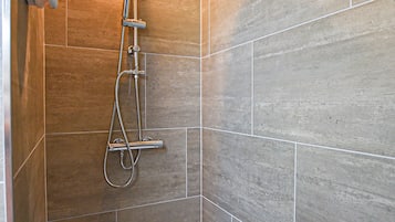 A shower with a handheld showerhead and a wall-mounted faucet.