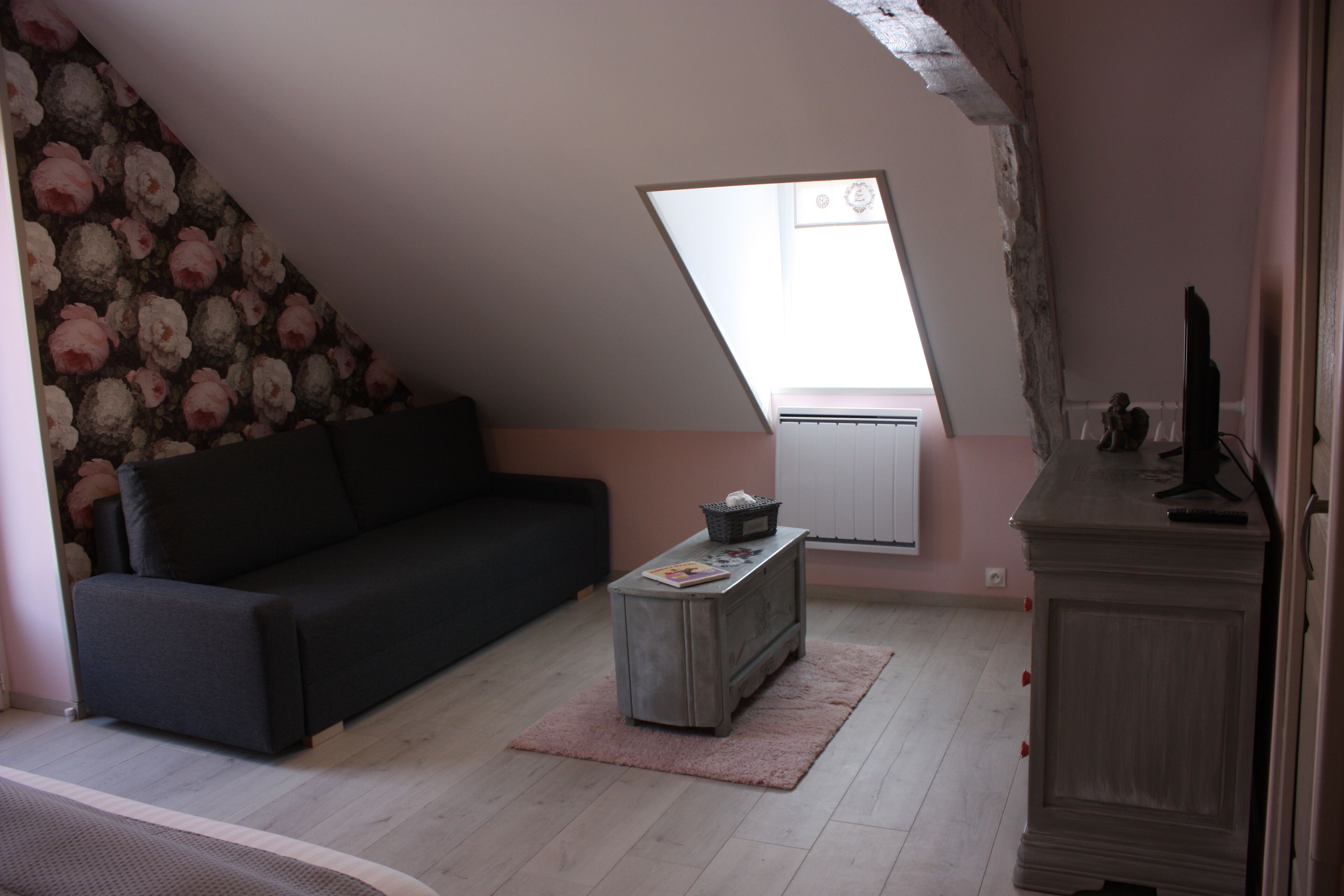 Ein Zimmer mit einer schwarzen Couch, einem kleinen Holztischchen, einer Heizung und einer schrägen Decke mit einem Oberlicht.