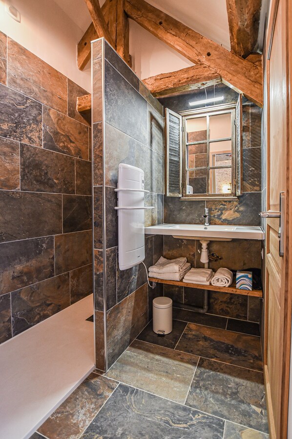 Un baño con baldosas de piedra, un lavabo blanco, un espejo y un perchero para toallas.