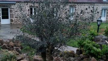 A stone building with a tiled roof, a small tree in the foreground, and a stone pathway leading to the entrance.