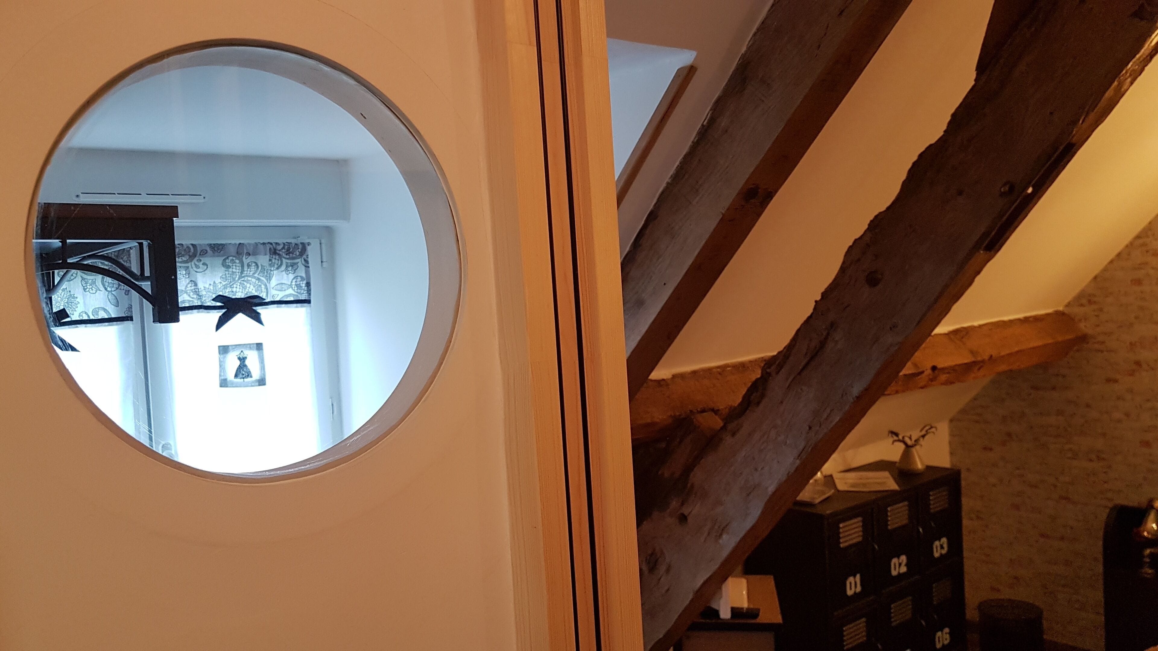 Una ventana circular con vistas a una habitación, vigas de madera y varios módulos de almacenamiento negros.