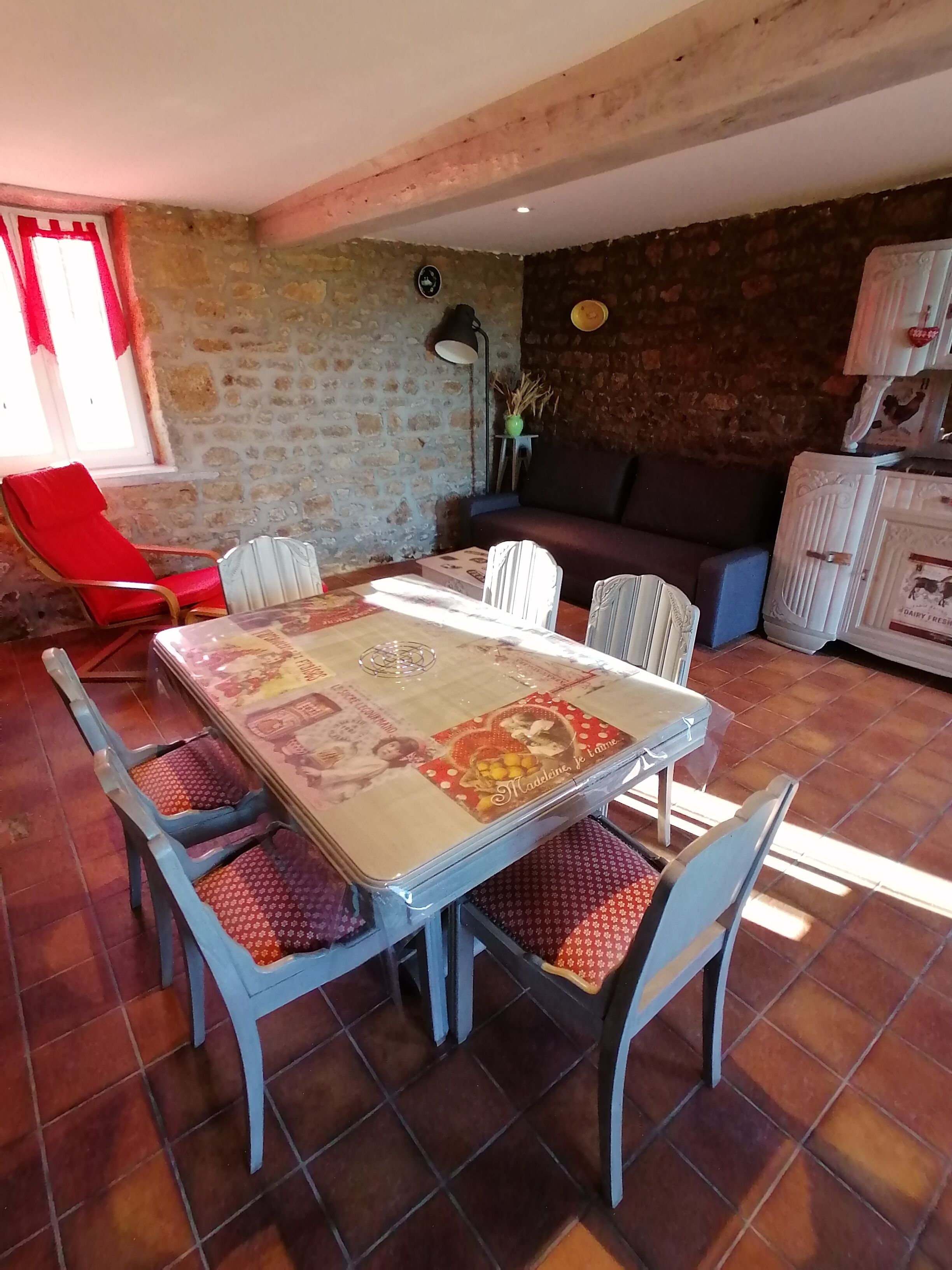 Un coin repas avec une table et des chaises, un fauteuil rouge, un canapé et un mur en pierre.