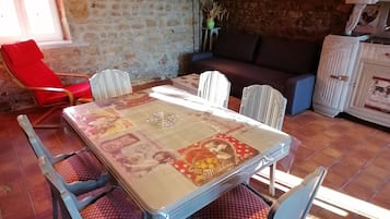 Un coin repas avec une table et des chaises, un fauteuil rouge, un canapé et un mur en pierre.
