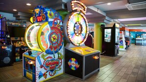 A brightly lit arcade with various gaming machines, including a spinning wheel game and a claw machine.