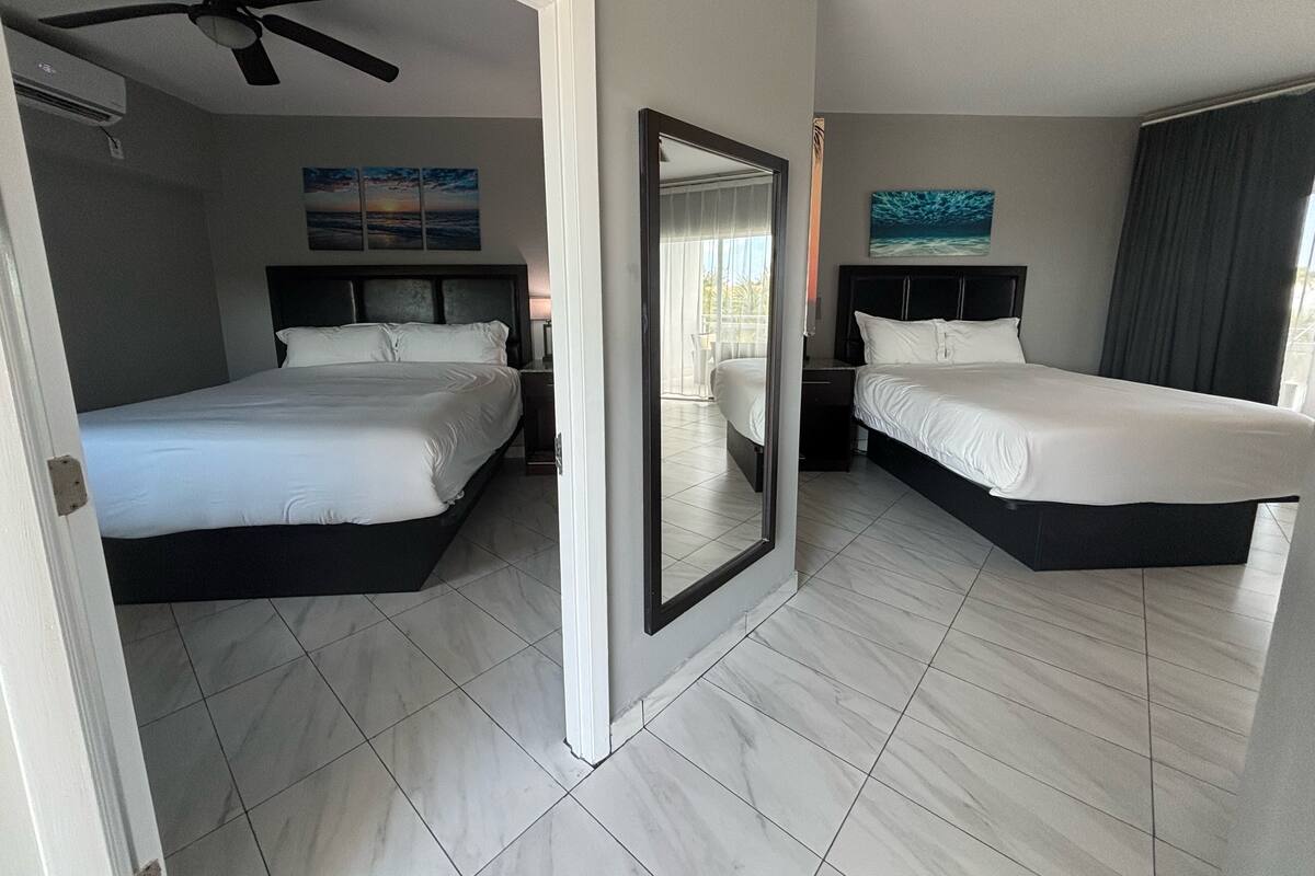 A hotel room with two beds, a ceiling fan, and artwork on the walls.