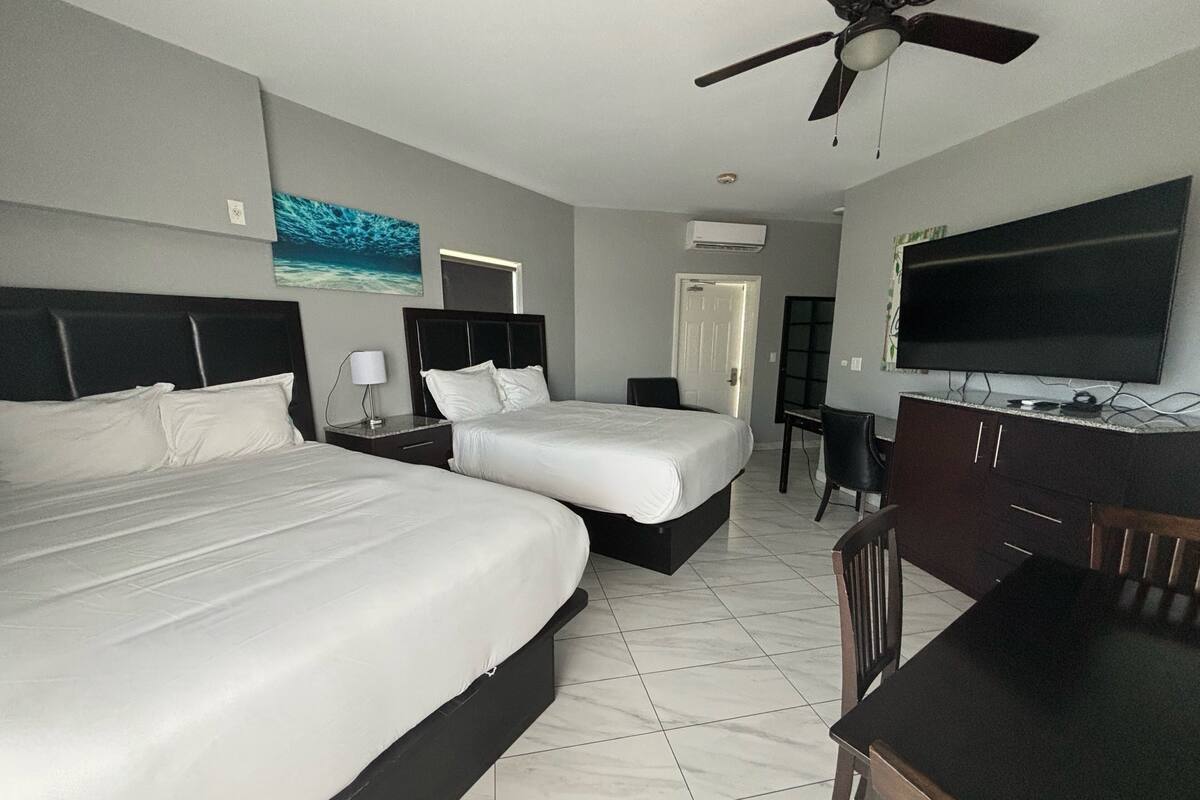 A hotel room with two beds, a desk, a chair, a television, and a ceiling fan.