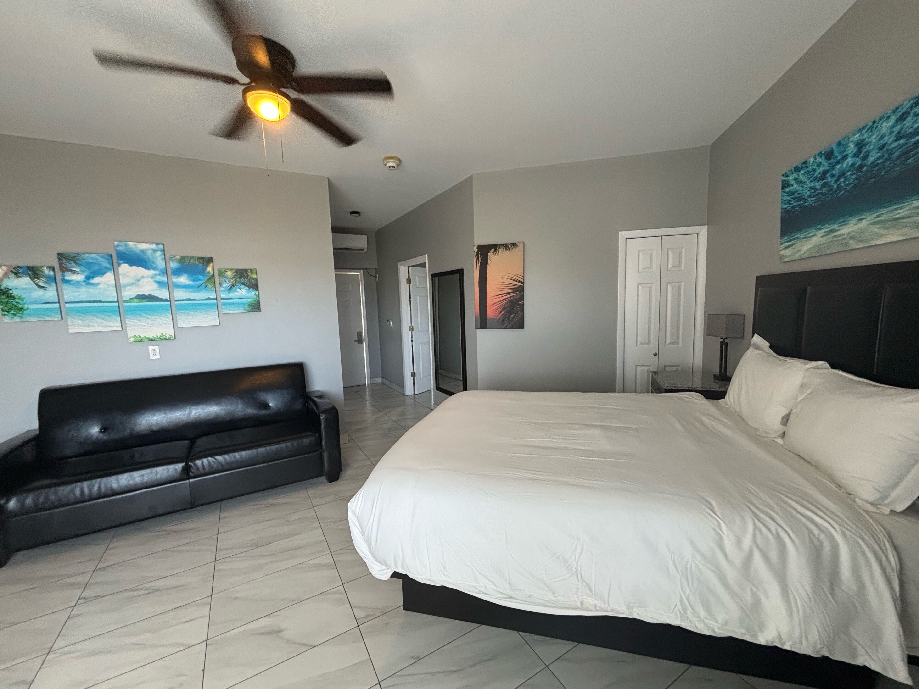 A bedroom with a large bed, a black leather sofa, and a ceiling fan.