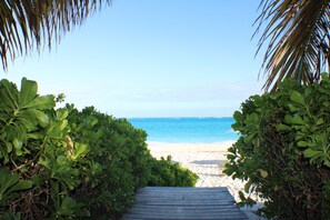 A pathway leading to a beach with clear blue water and white sand.